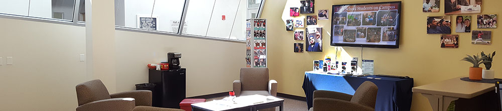 Welcome center, has some chairs around a table with many photos of students on the wall.