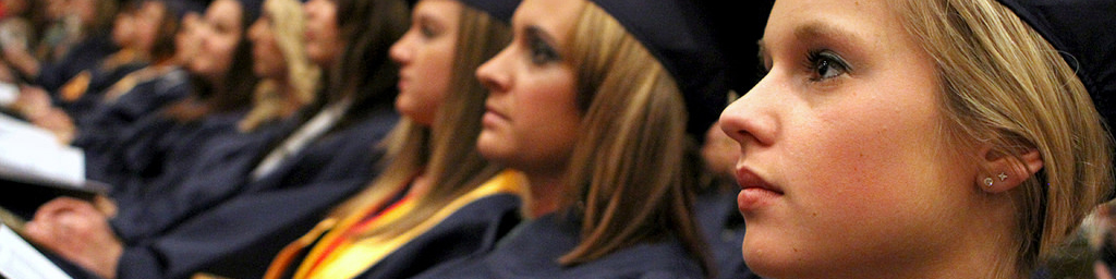 students in graduation cap and gown, sitting during graduation ceremony.